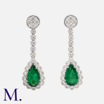 A Pair Of Emerald & Diamond Drop Earrings in 18k white gold, each comprising a round cut diamond set