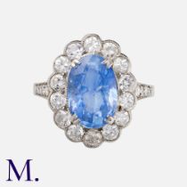A Sapphire And Diamond Cluster Ring in platinum, set with a principal oval cut blue sapphire of