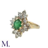 An Emerald And Diamond Cluster Ring in 14k yellow gold, set with a central oval shaped emerald of