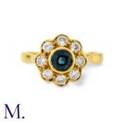 A Sapphire And Diamond Cluster Ring in 18k yellow gold, set with a principal round cut sapphire