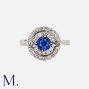 An Art Deco Sapphire And Diamond Cluster Ring in platinum, set with a principal round cut sapphire