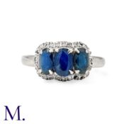 A Sapphire And Diamond Ring in 14k white gold, set with three oval cut sapphires within a round