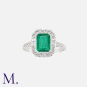 An Emerald And Diamond Cluster Ring in 18k white gold, set with a principal octagonal cut emerald of