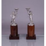 A pair of silver candlesticks in the shape of torch-bearing putti (BWG), mounted on a polished woode