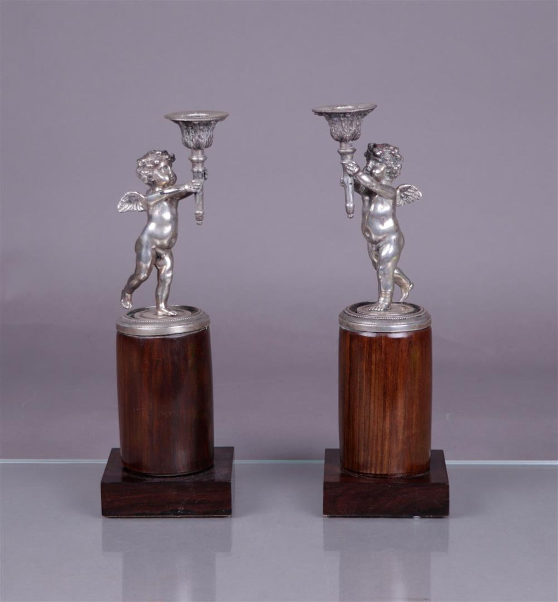 A pair of silver candlesticks in the shape of torch-bearing putti (BWG), mounted on a polished woode