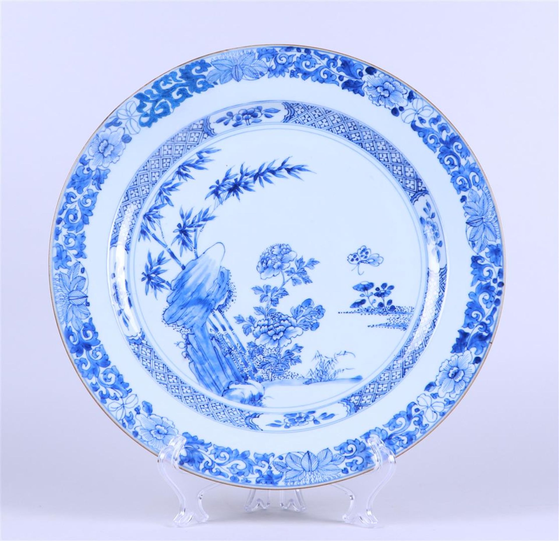 A porcelain dish with rich floral decoration near a rock with butterfly, outer edge with floral deco
