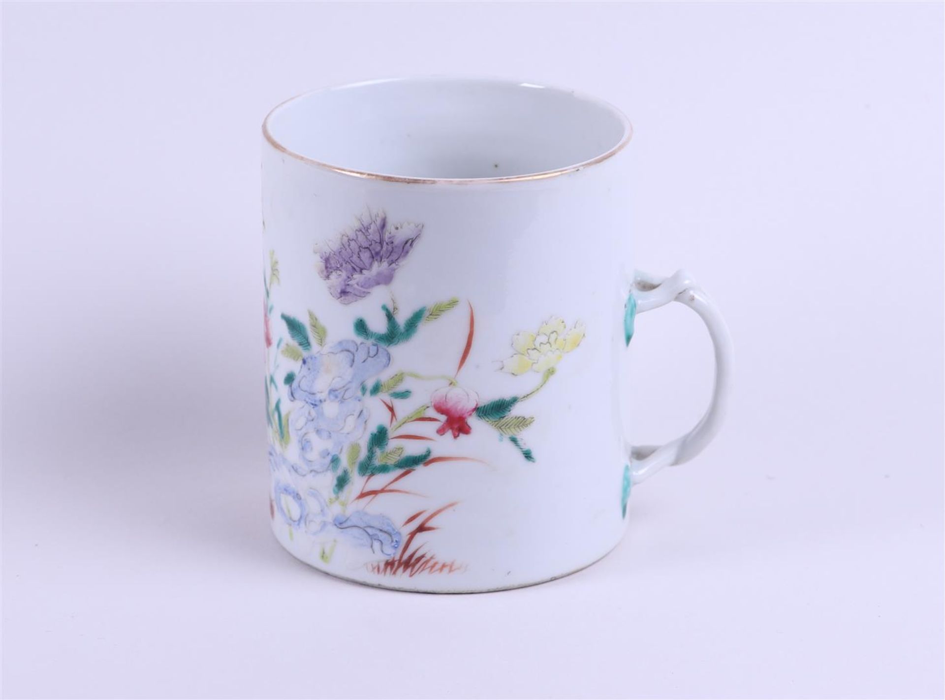 A porcelain Famille Rose cup with woven handle with rich floral decoration on rock decor with bird a