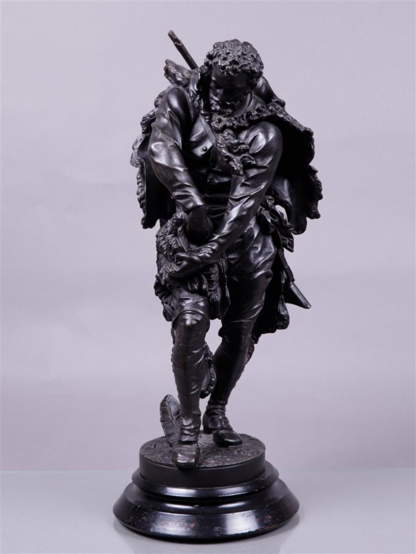 A dark patinated metal statue on a wooden base of a hunter storing a bird in a hunting bag. 19th cen