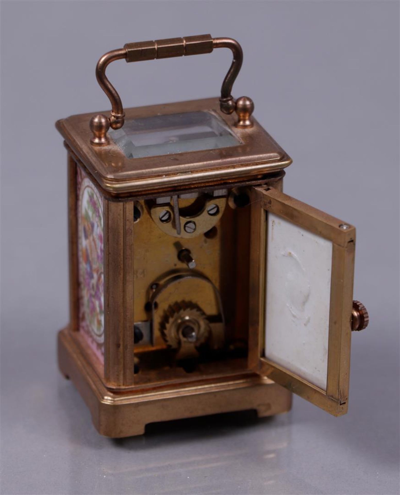 A brass travel alarm clock with polychrome decorated plaques, 20th century.
H.: 5,5 cm. - Image 2 of 2