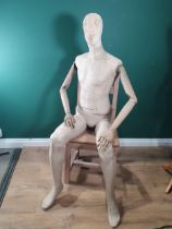 A seated male Shop Mannequin with fabric covered head, torso and legs and wooden arms, with