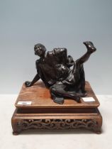 A Chinese bronze Sculpture of a man in robes falling over, on associated hardwood Stand 6 1/2in H