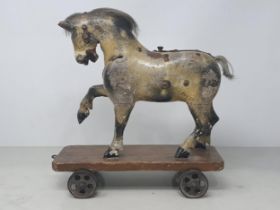 An antique carved and dapple painted pull along Horse on stained wooden base with metal wheels
