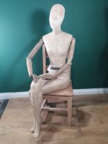 A seated female Shop Mannequin with fabric covered head, torso and legs and wooden arms, with
