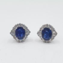A pair of Sapphire and Diamond Cluster Earrings each claw-set oval-cut sapphire within a frame of