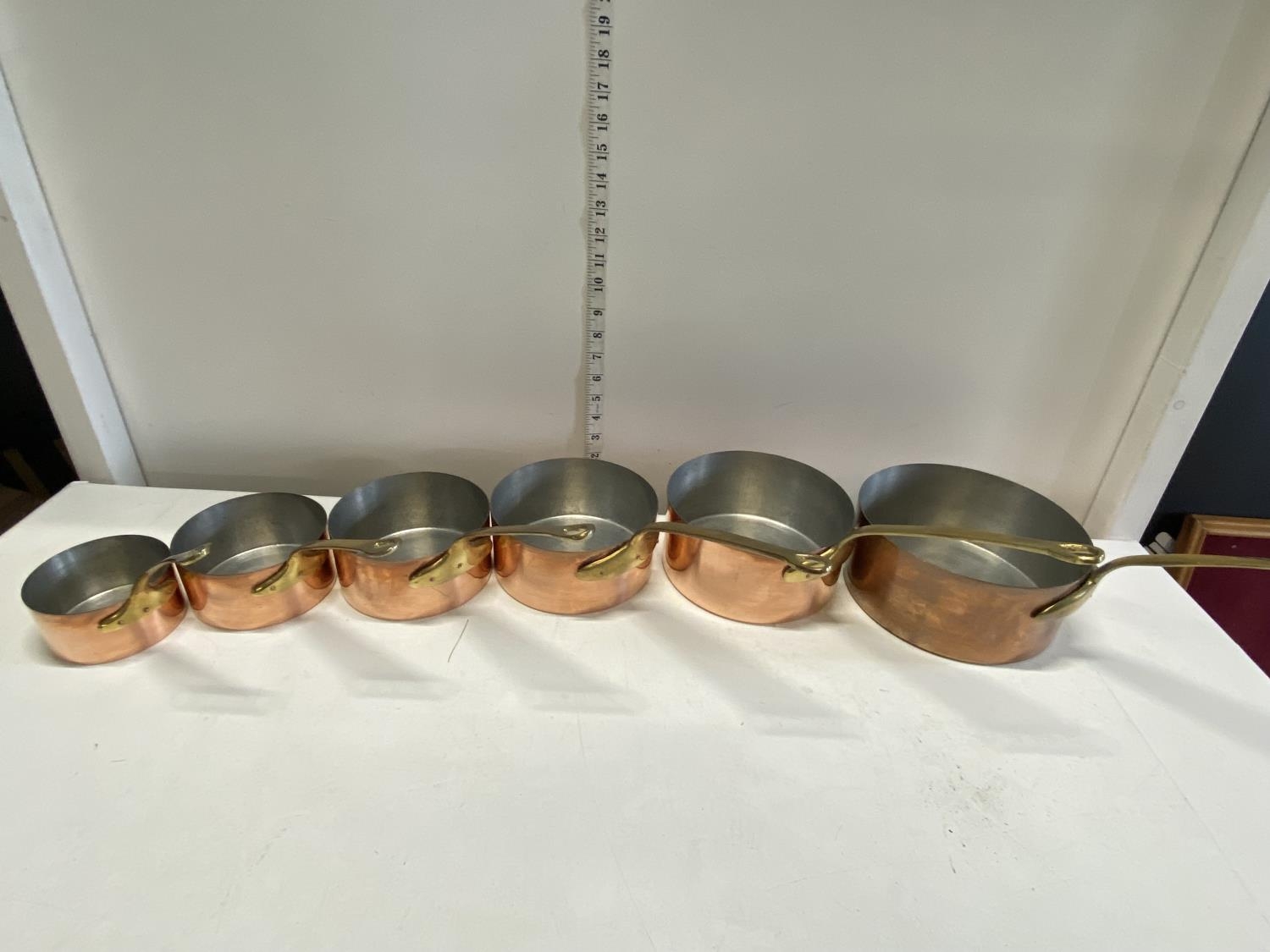 Six antique graduated copper and brass saucepans