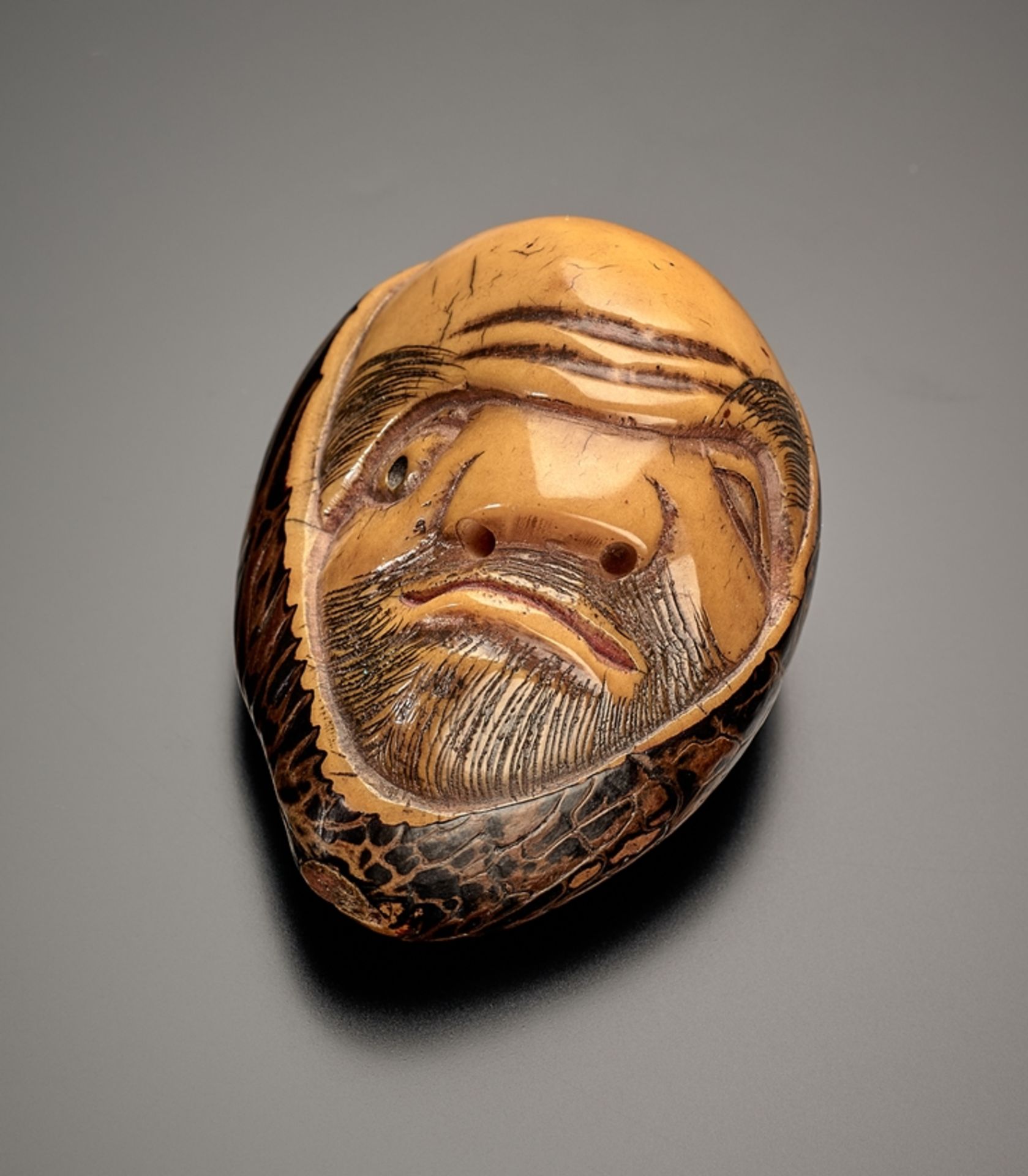 Netsuke. Ungewöhnliches Gesicht. Steinnuss, signiert Masatama. Rückseitig zwei kleine Himotoshi. H