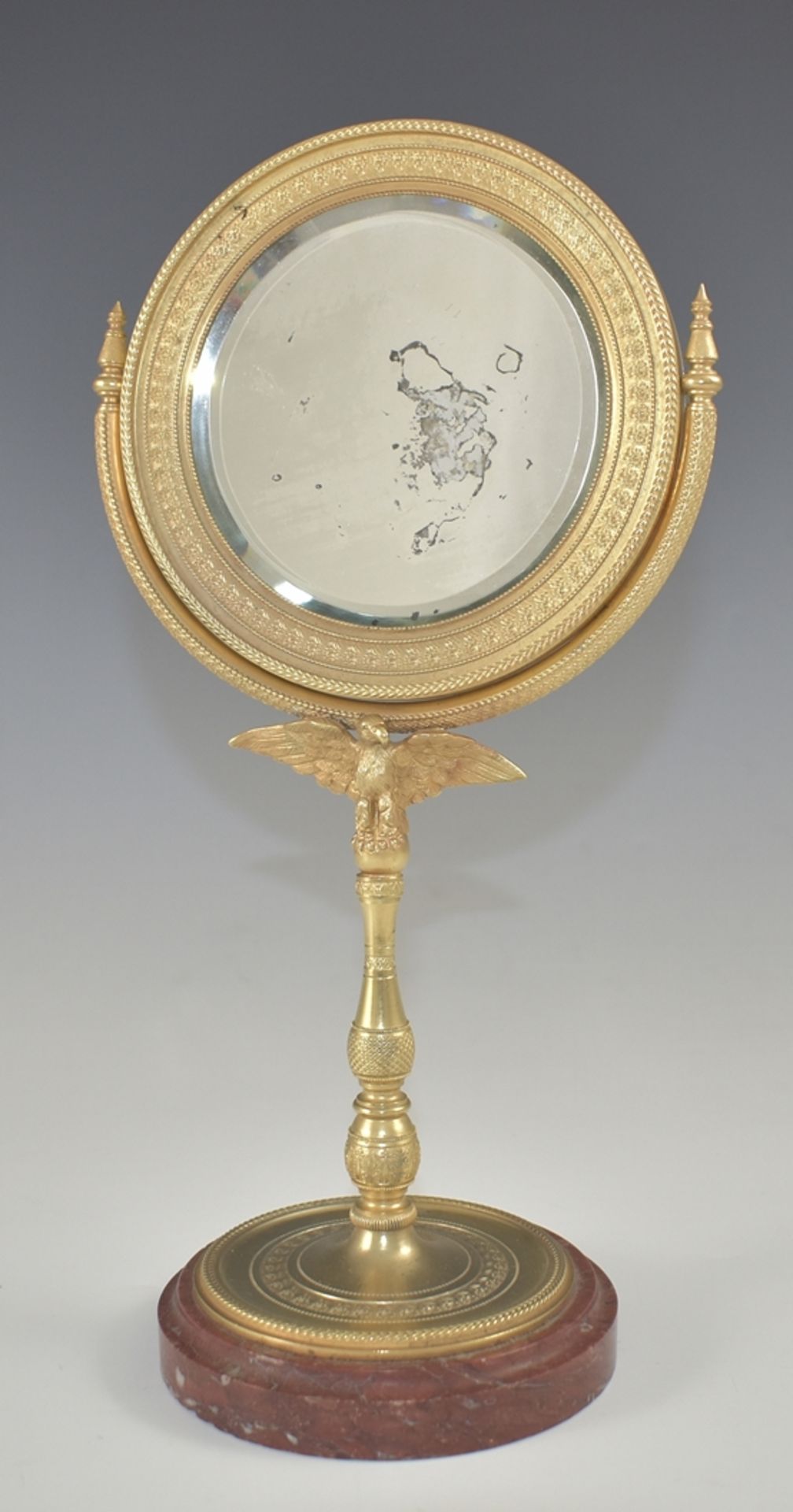 Empire-Standspiegel. Säulenschäftung mit Adlerhalterung und rundem Spiegel. Feiner Reliefdekor mit 
