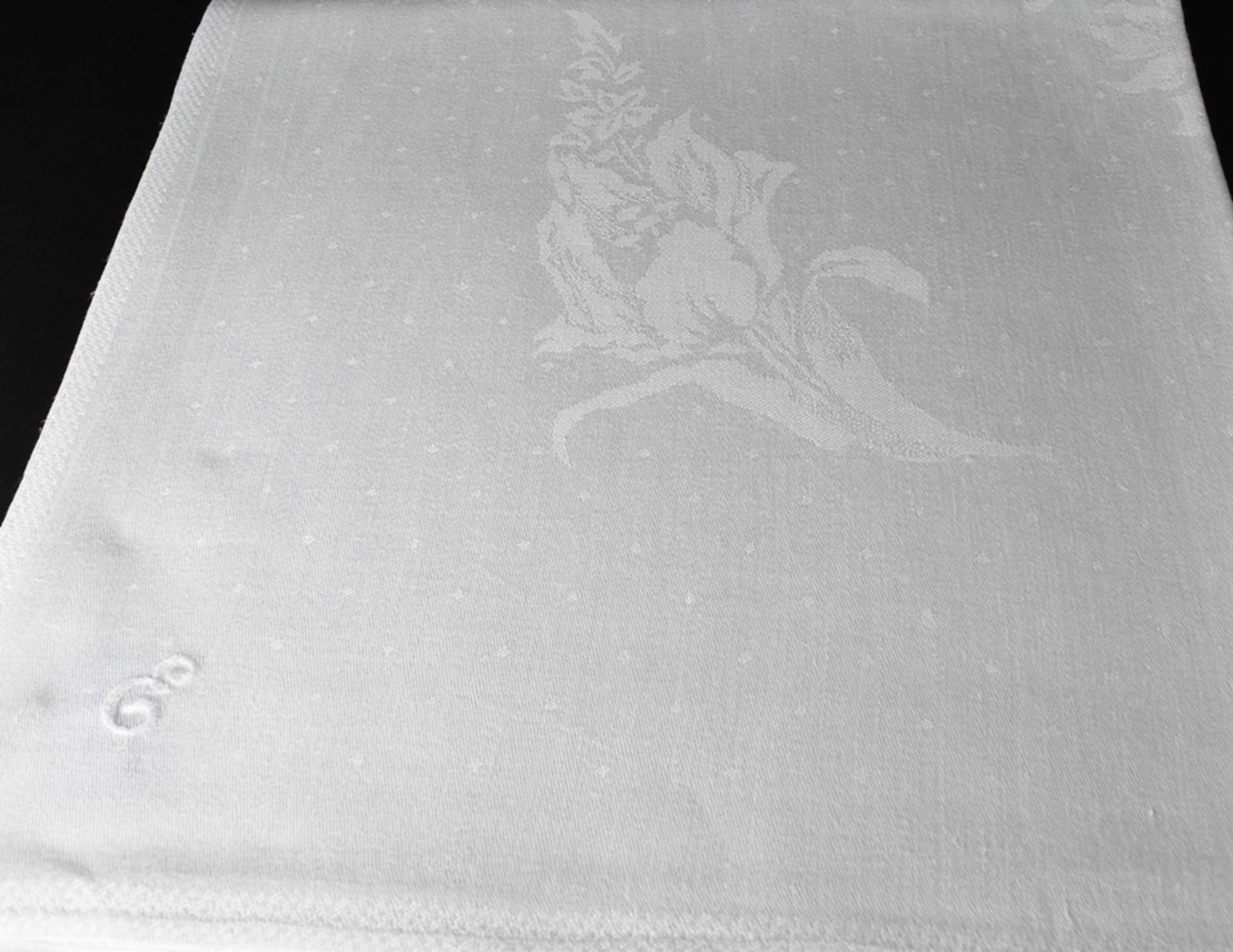 Tischtuch mit einem Doppeloval aus Blütengirlanden und Monogramm E. Leinendamast. In den Ecken groß
