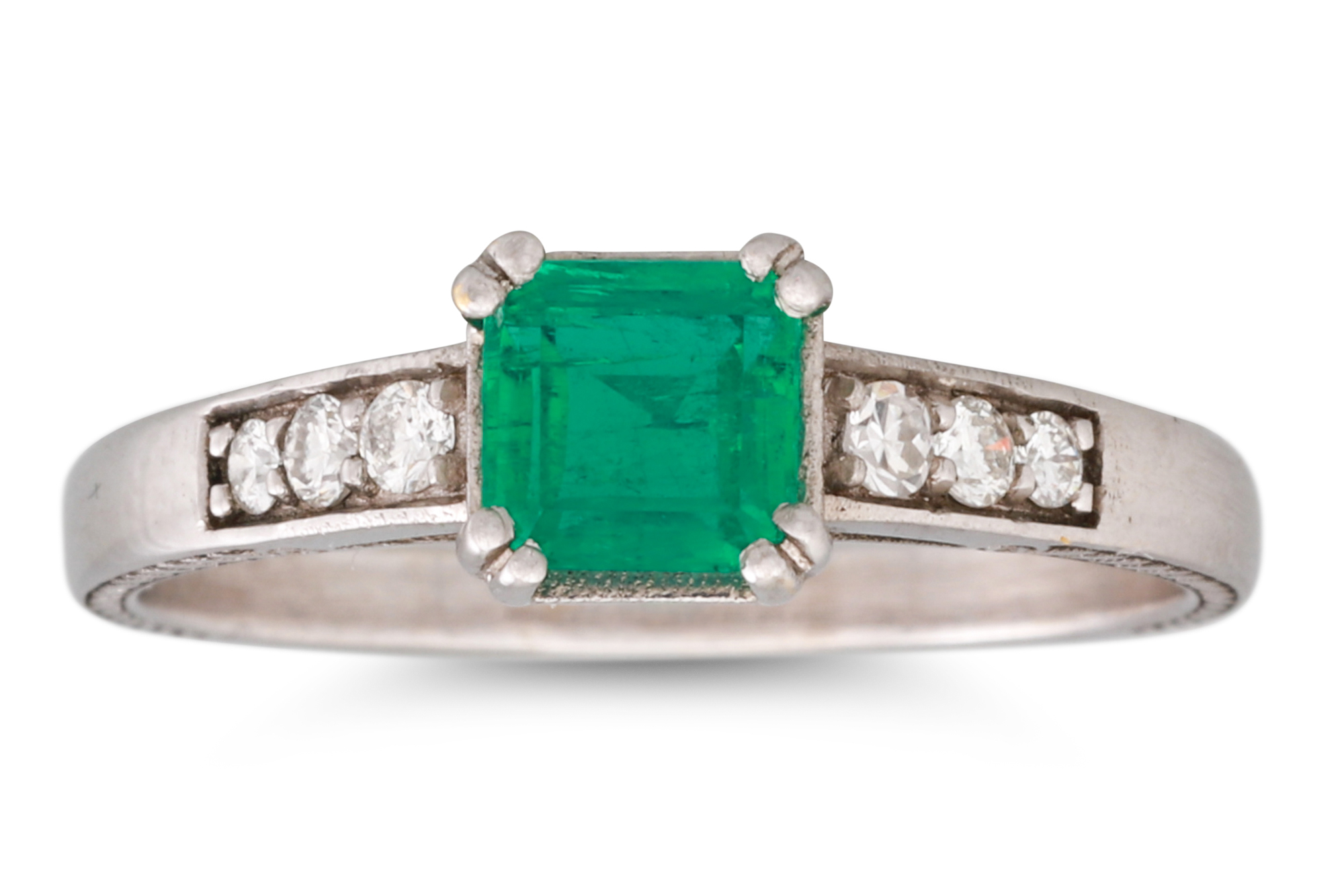 A COLOMBIAN EMERALD AND DIAMOND SET RING, the trap cut emerald to diamond shoulders, mounted in