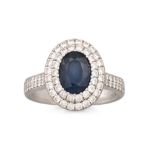 A SAPPHIRE AND DIAMOND CLUSTER RING, the oval sapphire to a two rowed diamond halo surround, to