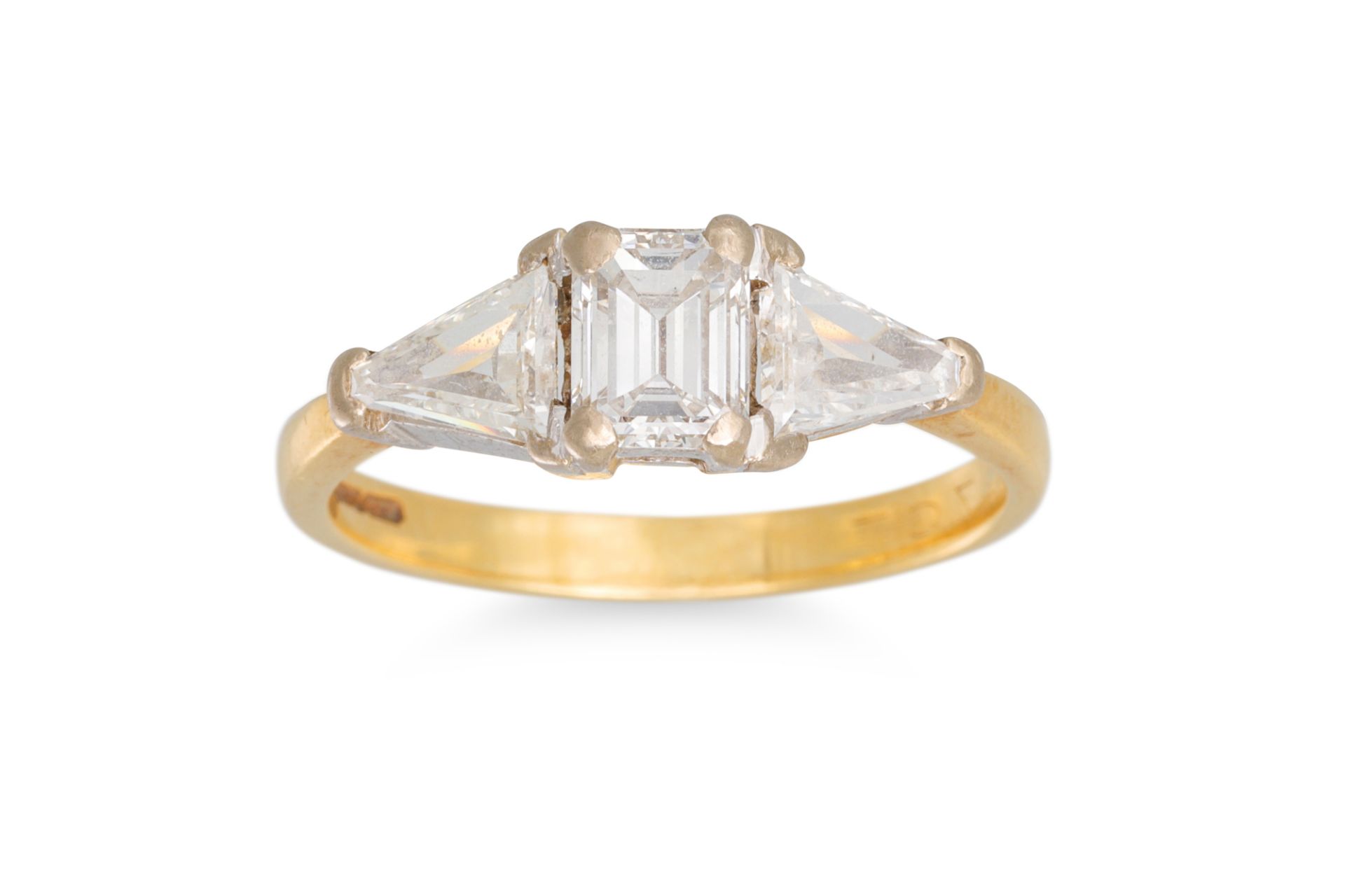 AN EMERALD CUT DIAMOND RING, with trillion shoulders, mounted in yellow gold. Estimated: weight of