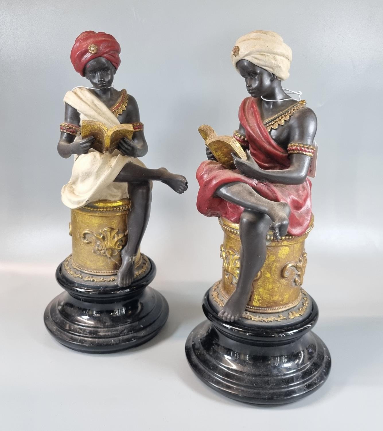 Pair of polychrome and gilt composition blackamoor figures of young boys sitting on pedestals,