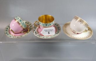 A pair of Royal Worcester pink ground and gilded cups and saucers with repeating floral and