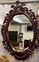 Modern hardwood bevelled mirror of oval form, the frame decorated with flowers, fruits and