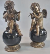 Pair of bronze seated musical cherubs playing the flute and harp, on glass globular and gilded