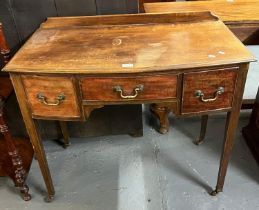 Edwardian mahogany bow front side table/desk having three drawers on tapering legs and casters. (B.