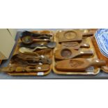 Two trays of carved wooden items to include: oriental design butter pats, scoops and cutlery,