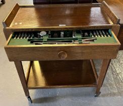 Early 20th century oak two tier trolley on wheels, the pull out drawer with a collection of silver