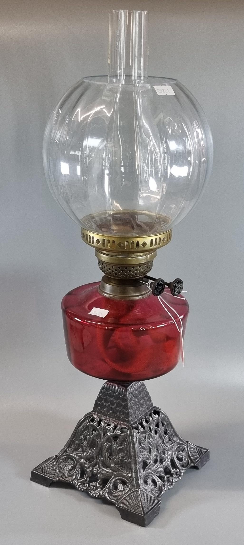 Early 20th century double oil burner lamp having glass globular shade above a cranberry glass