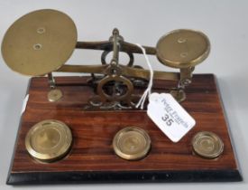 Set of brass postal scales with one, two and four ounce brass weights on a stained wooden base. 20cm