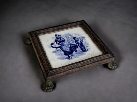 A PAINTED DELFT TILE TRIVET STAND. 19th Century. Wood framed, with gilt metal Lion paw feet. 5 x