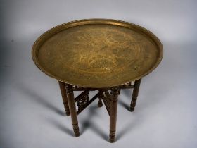 A PERSIAN BENARES BRASS TRAY TABLE. With fold down carved legs and Islamic style design to large