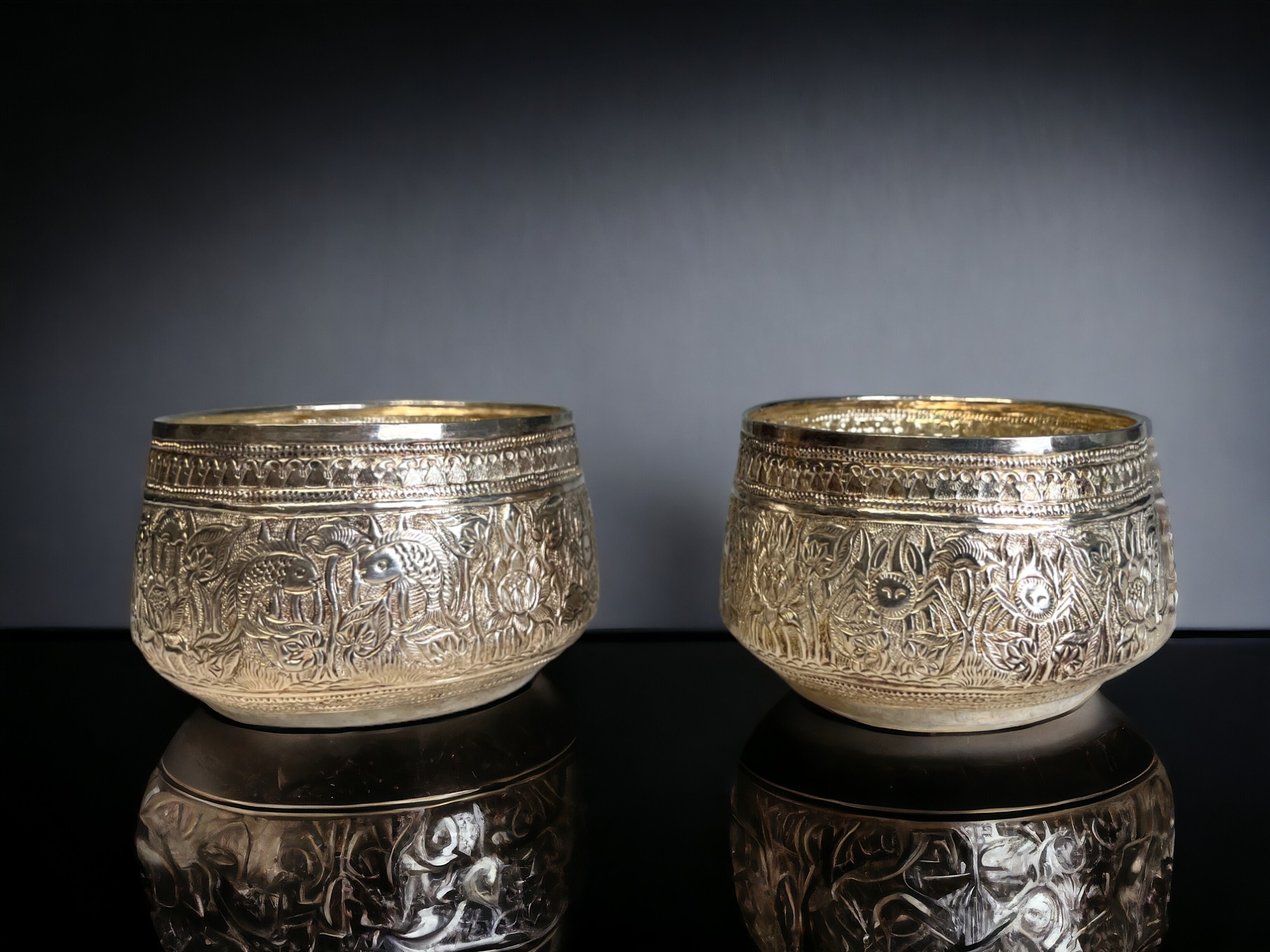 A PAIR OF BURMESE SILVER THABEIK BOWL. Repousse decorated with fish and crabs amongst stylised