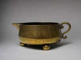 A Victorian brass milk jug. Squat body, with engraved foliate ornament. On three ball feet.