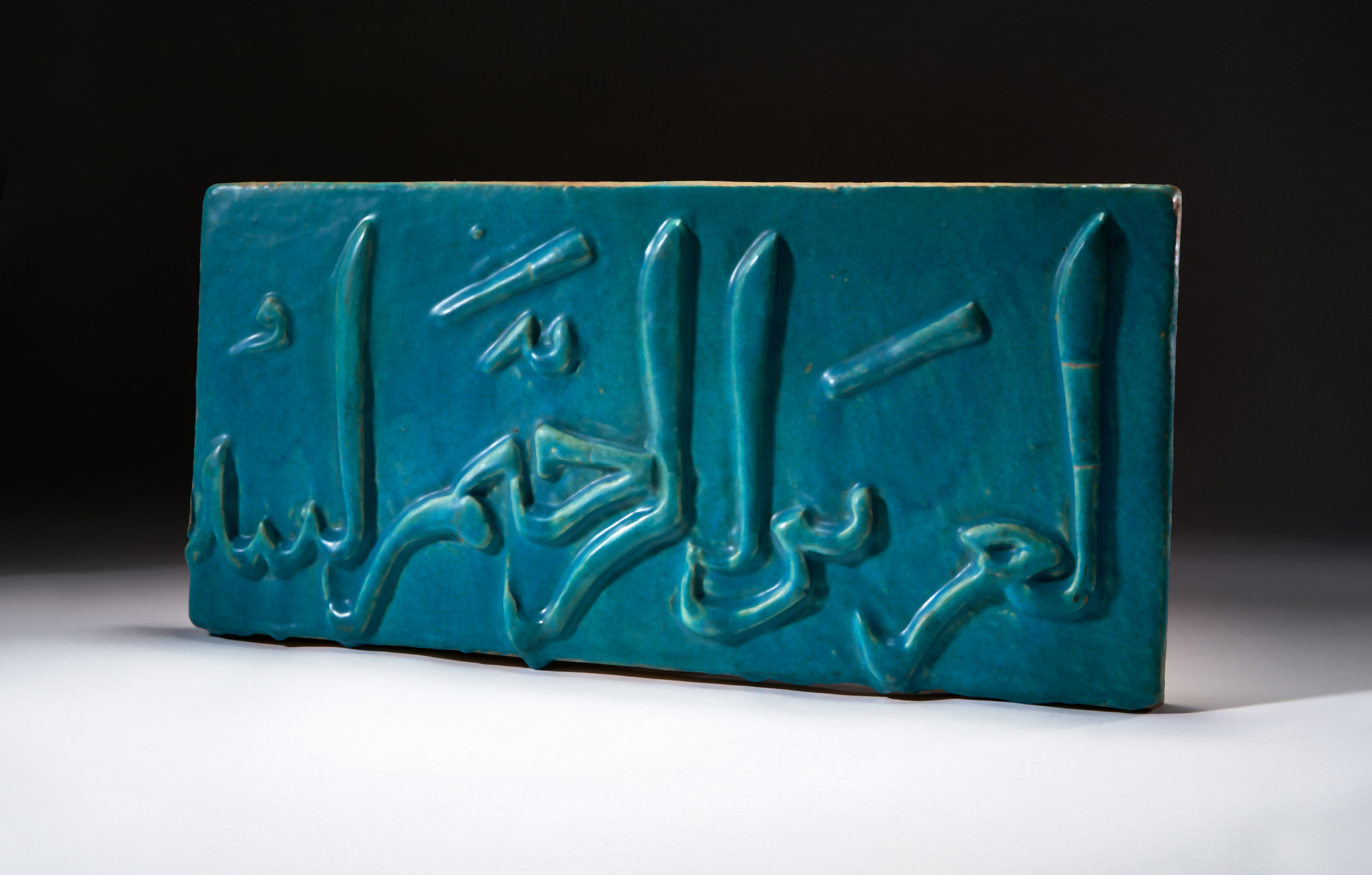 A TURQUOISE GLAZED CALLIGRAPHY TILE, KASHAN, CIRCA 12TH CENTURY, PERSIA