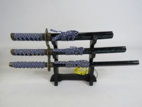 Set of three Ancient Warrior small decorative swords with wooden stand, longest measures 31cm.