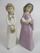 2 Nao figurines of girls, one holding a dove and one holding a basket. The tallest stands 27cm.