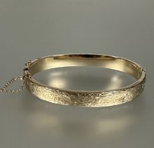 A 9ct gold hollow stiff hanged bangle with engraved decoration and safety chain, no signs of repairs
