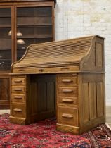 An early 20th century oak serpentine roll top desk, the tambour front opening to reveal a fitted