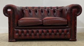 A vintage two seat Chesterfield sofa, upholstered in deep buttoned oxblood red leather, moving on