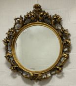 An ornate circular gilt composition framed wall mirror in the Rococo taste, the frame decorated with