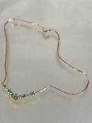 A 9ct gold V shaped necklace set five oval cut emeralds in open work mount set diamond points on