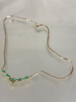 A 9ct gold V shaped necklace set five oval cut emeralds in open work mount set diamond points on