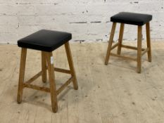 A pair of mid 20th century beech stools, each with faux leather seat raised on splayed supports.