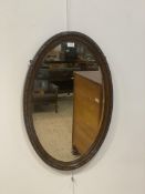 An early 20th century oval wall hanging mirror in a carved oak frame. 80cm x 52cm.