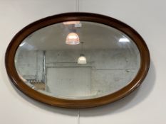 An early 20th century oval wall hanging mirror, the mahogany frame enclosing a bevelled plate 83cm x